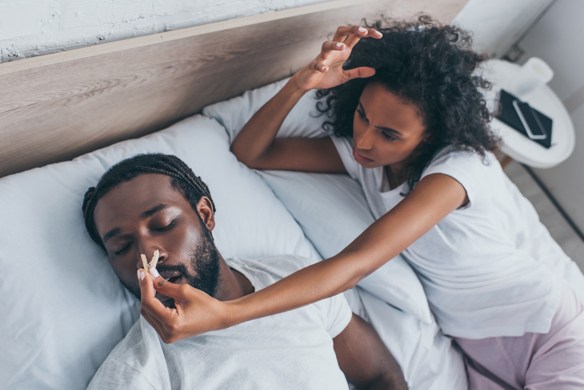 young african american woman pinning nose of snoring husband